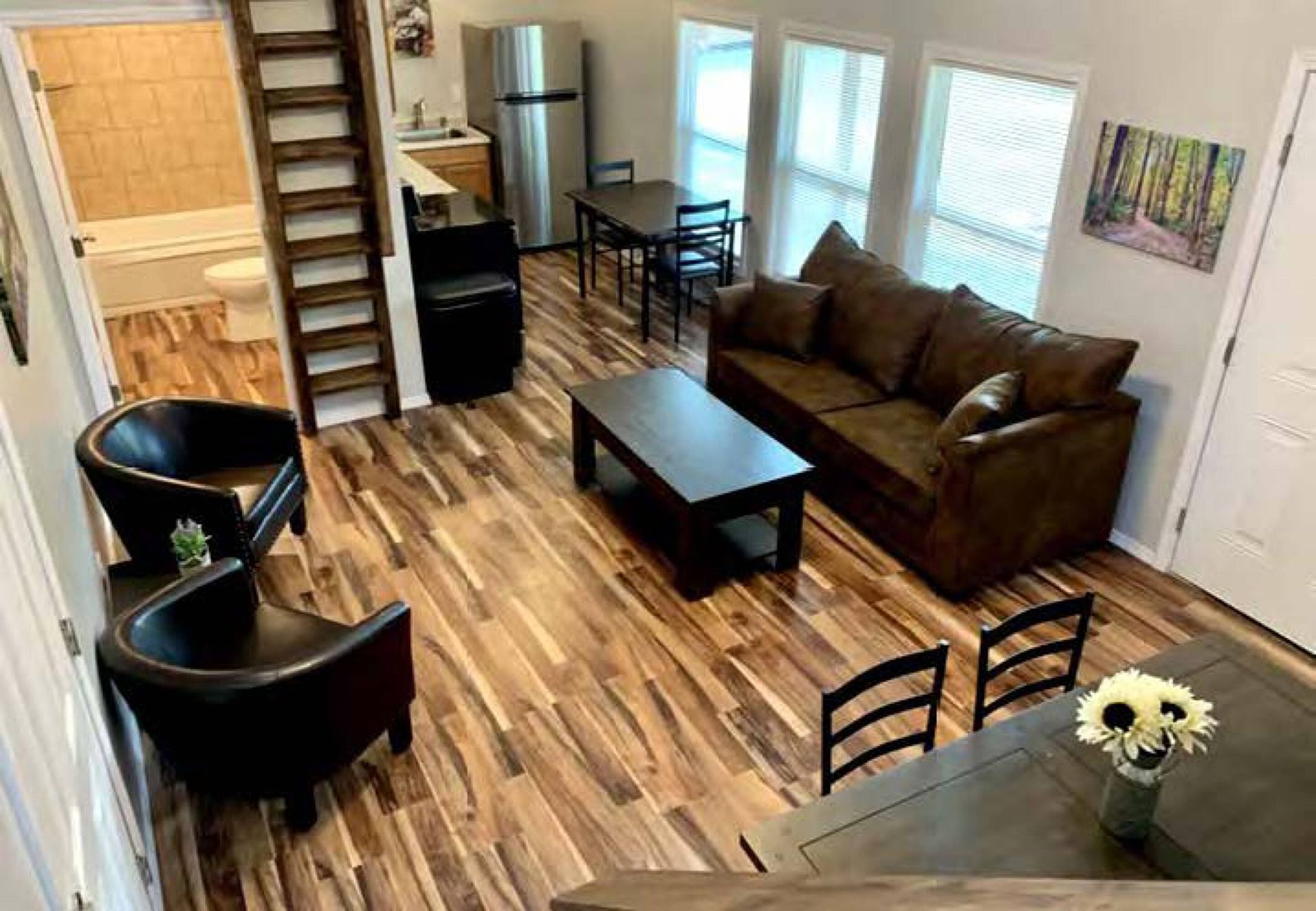 Modern loft living room with brown sofa, black chairs, coffee table, stairs, and dining area