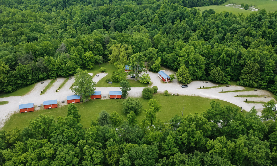 Aerial view of a forest campground with colorful cabins beside a curved road and parking area.