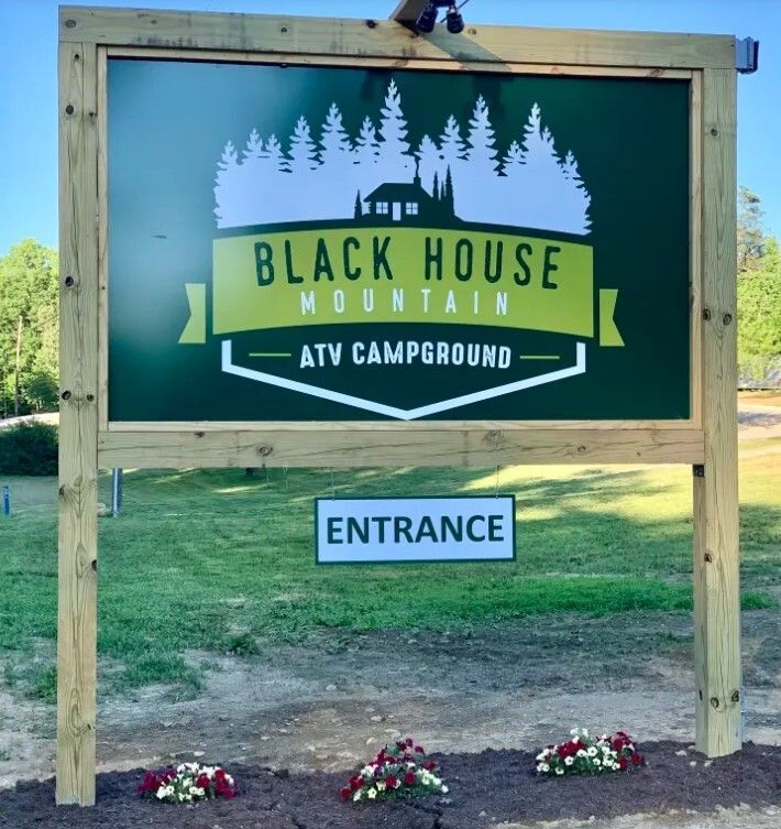 Black House Mountain ATV Campground entrance sign with flowers at the base