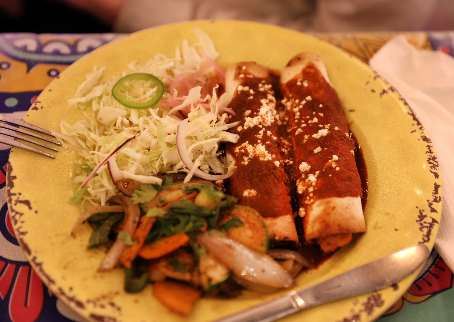 Plate of enchiladas with red sauce, rice, and vegetables on a yellow plate, garnished with lime.