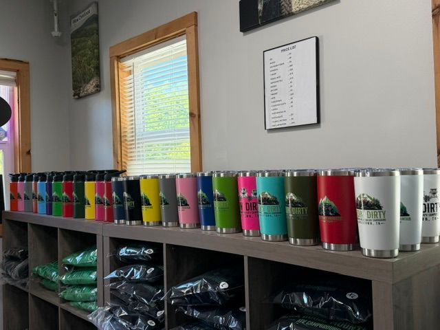 Colorful tumblers lined up on a shelf in a classroom or office, with storage bins below and a window behind