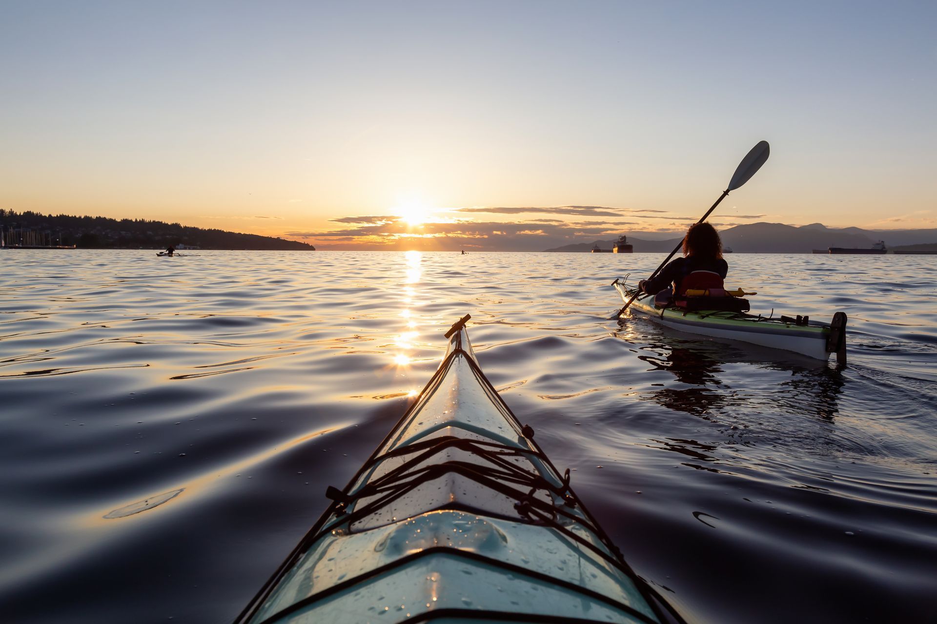 Kayakers on calm water at sunset, with a kayak in the foreground and another paddler to the right.