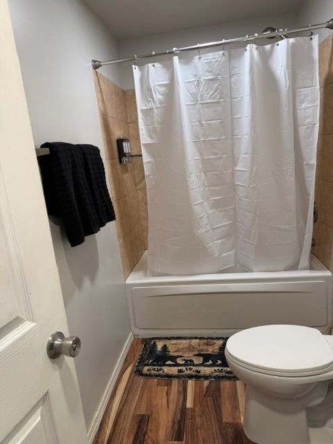 Small bathroom with white shower curtain, wood-look floor, toilet, and towel on the wall.