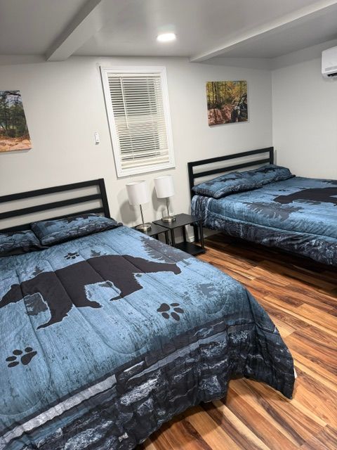 Bedroom with two beds, blue bear-print comforters, wooden floor, and wall art.