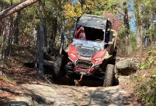 Red off-road vehicle climbing rocky forest trail between trees and boulders