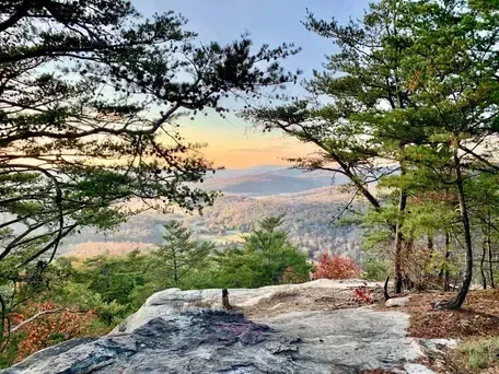 Sunset view from a rocky forest overlook across a hazy valley