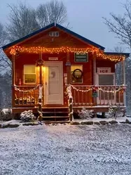 Small red cabin decorated with warm holiday lights in a snowy yard at dusk