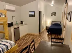Small studio apartment with kitchen, dining table, and bed in a narrow room with wood floors