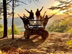 Group of people posing on an off-road vehicle at sunset in a forest clearing