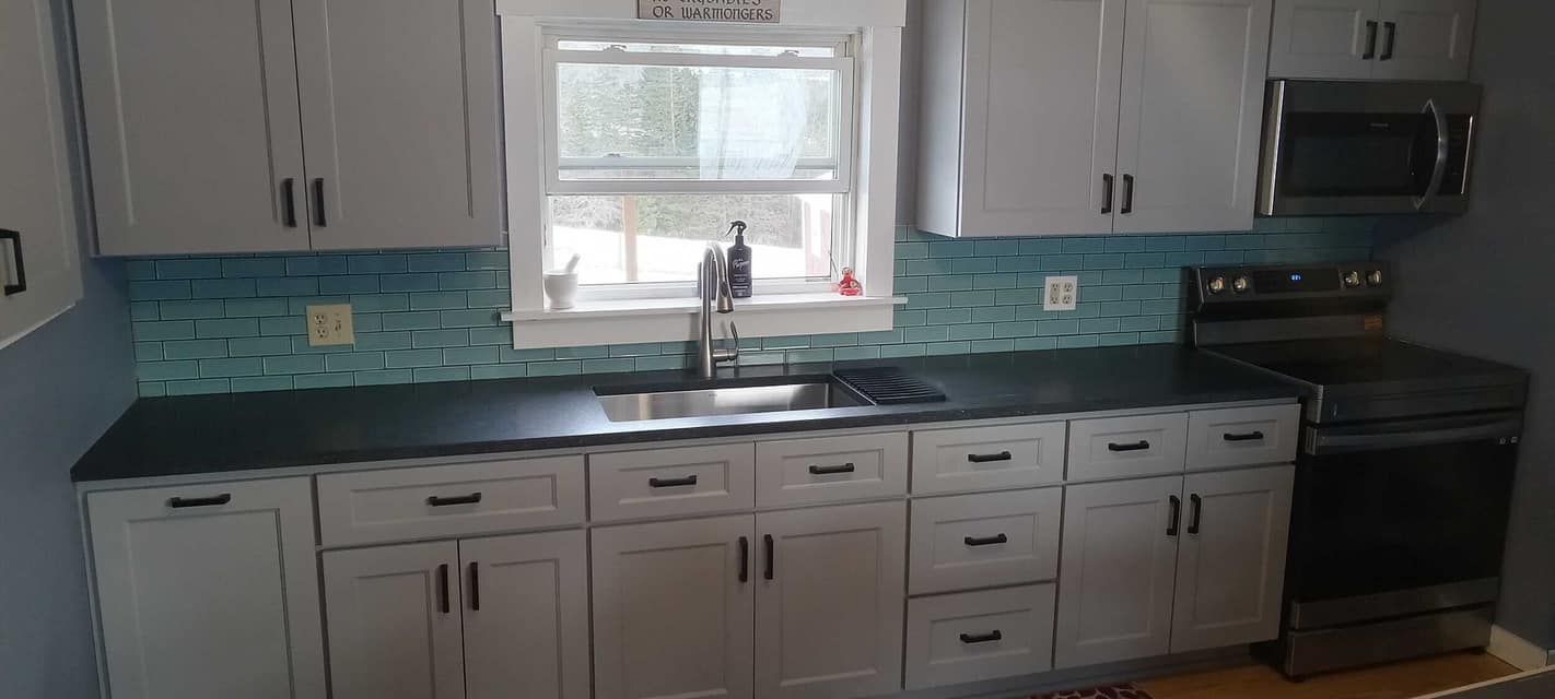 An updated modern kitchen remodel by Juggernaut Construction company in Vermont with white cabinet, grey countertops, and blue subway tile.