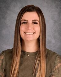 Smiling person with long straight hair against a gray studio backdrop.