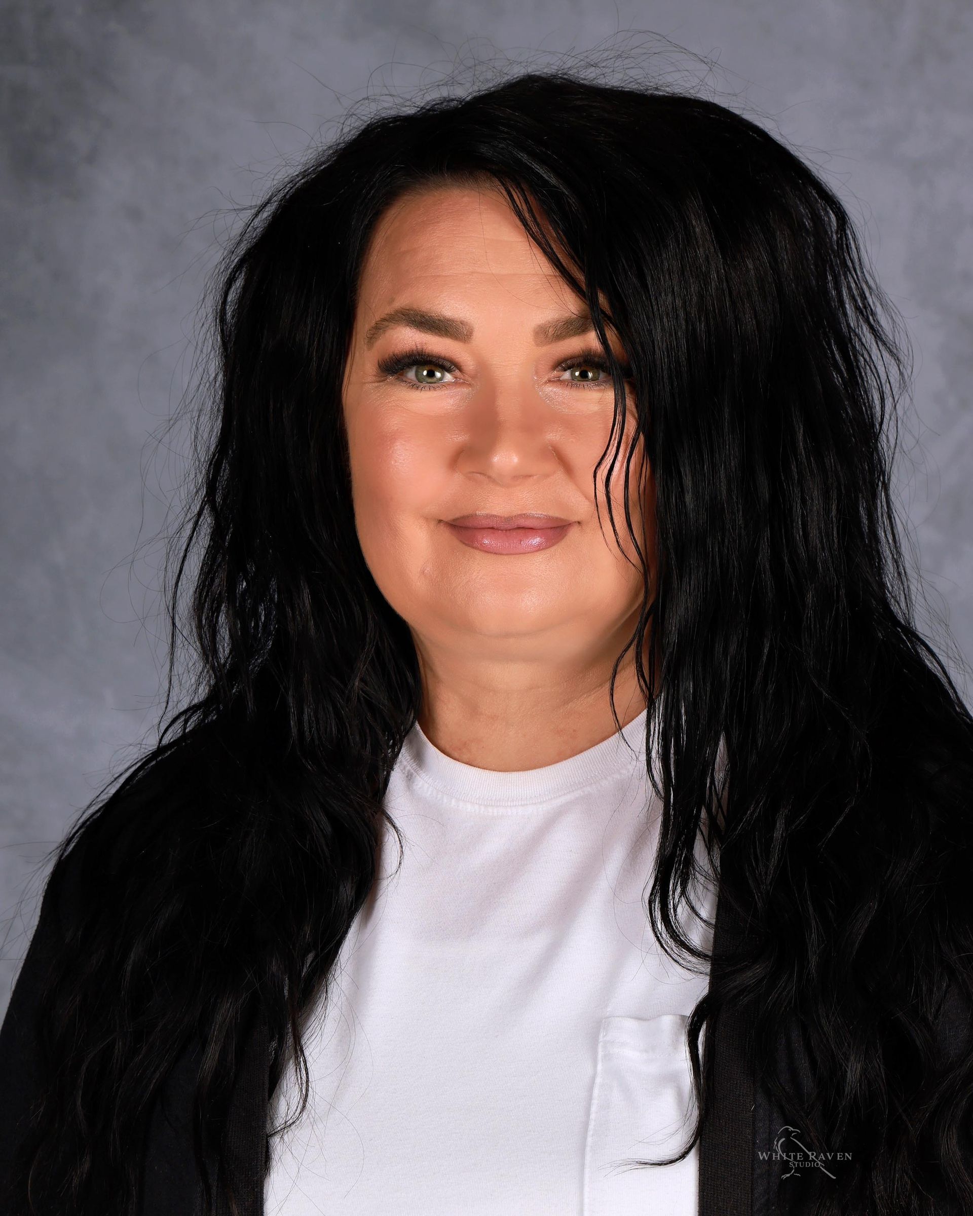Woman with long black hair, wearing a white shirt, smiling.