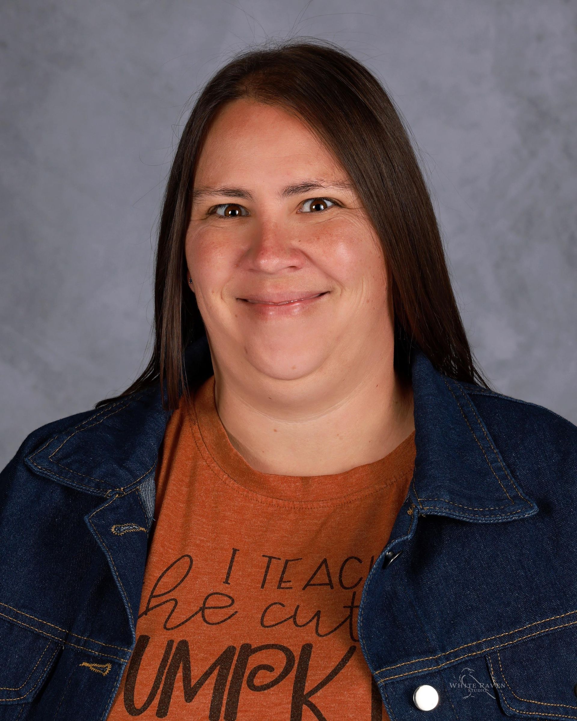 Woman wearing a denim jacket and orange t-shirt smiles; text on the shirt reads 