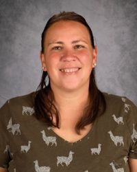 Smiling person in an olive shirt with llama pattern against a gray backdrop
