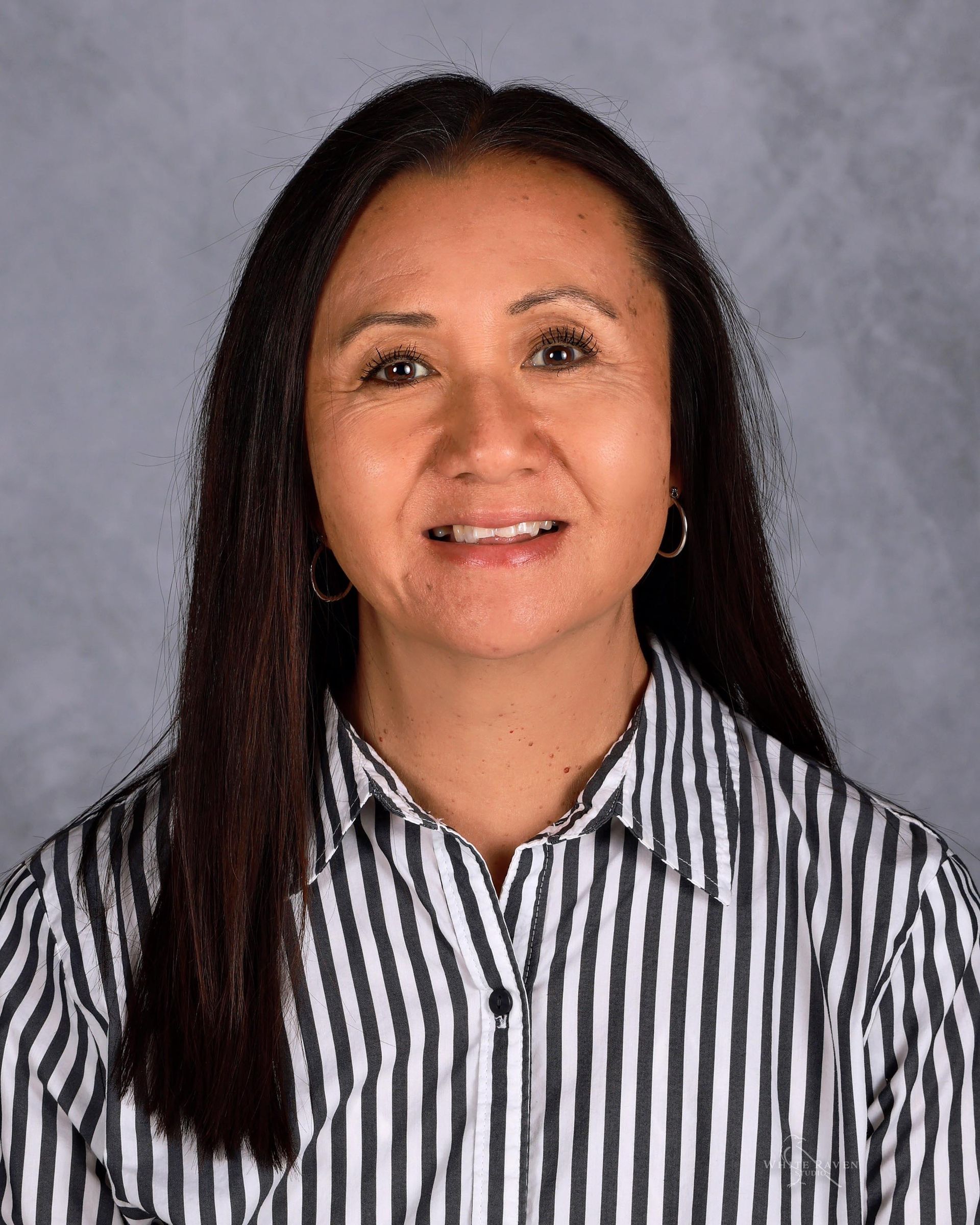 Woman with long dark hair, wearing a striped shirt, smiling.