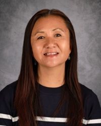 Portrait of a smiling person with long dark hair against a gray studio backdrop