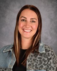 Smiling person in a denim jacket with a leopard-print top against a gray studio backdrop