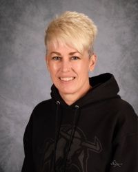 Person with short blond hair wearing a black hoodie, smiling against a gray studio backdrop