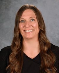 Smiling woman with long brown hair in a black top against a gray studio backdrop