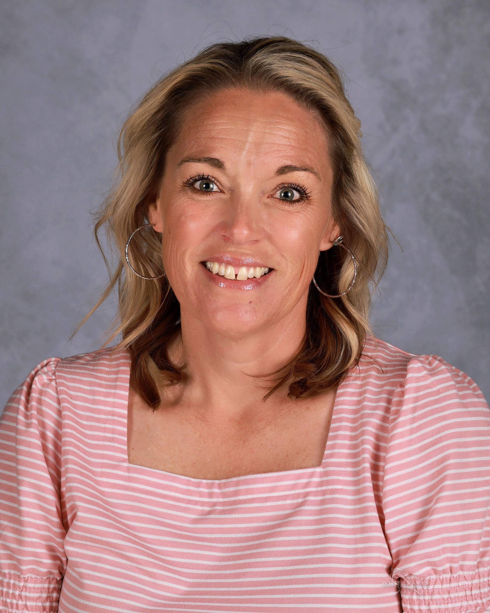 Woman with blonde hair wearing a pink and white striped shirt, smiling at the camera.