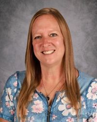 Woman smiling in a blue floral blouse against a gray studio backdrop