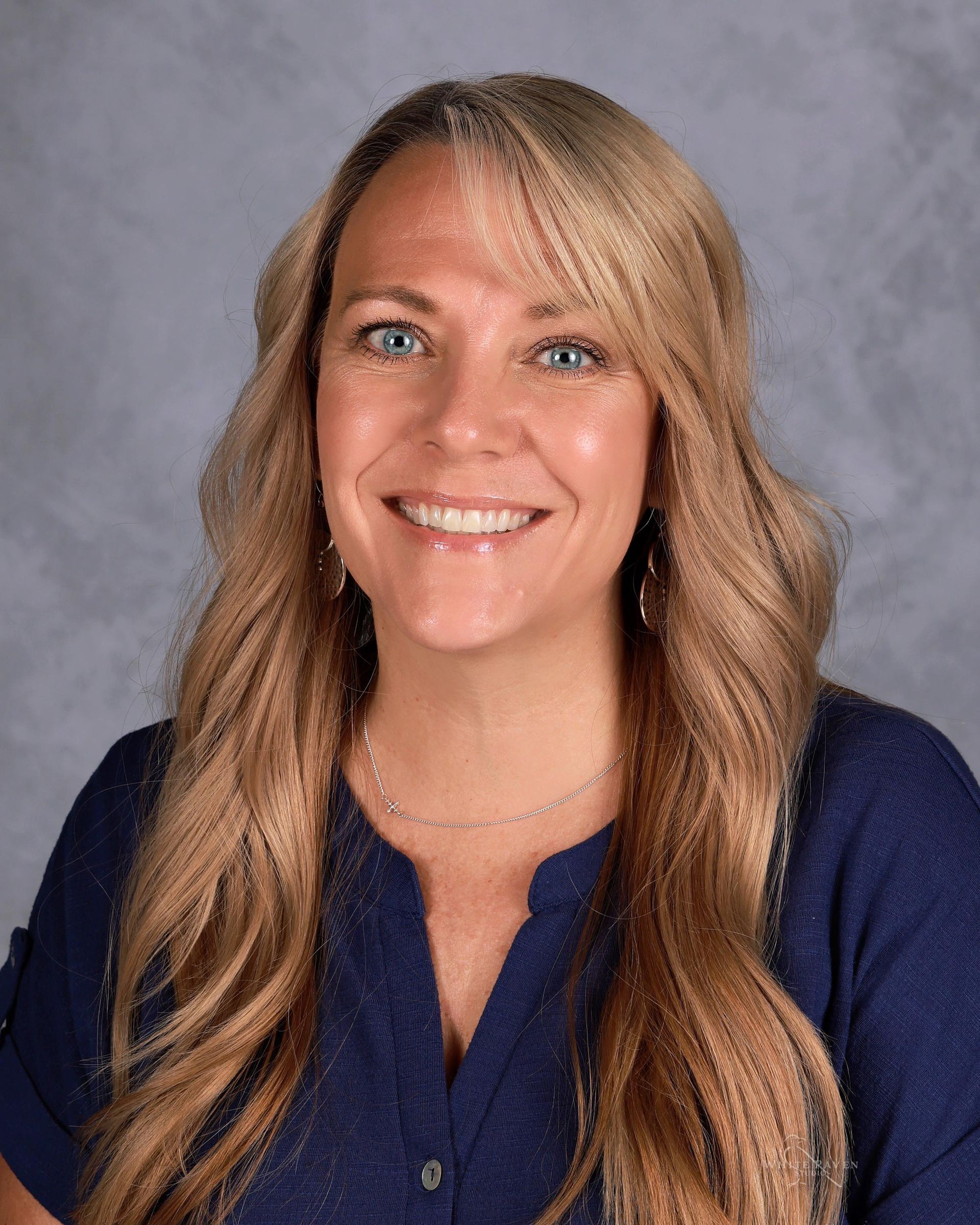Woman with blonde hair smiling, wearing a blue shirt.