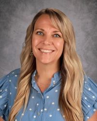 Smiling woman in a blue polka-dot shirt against a gray studio background