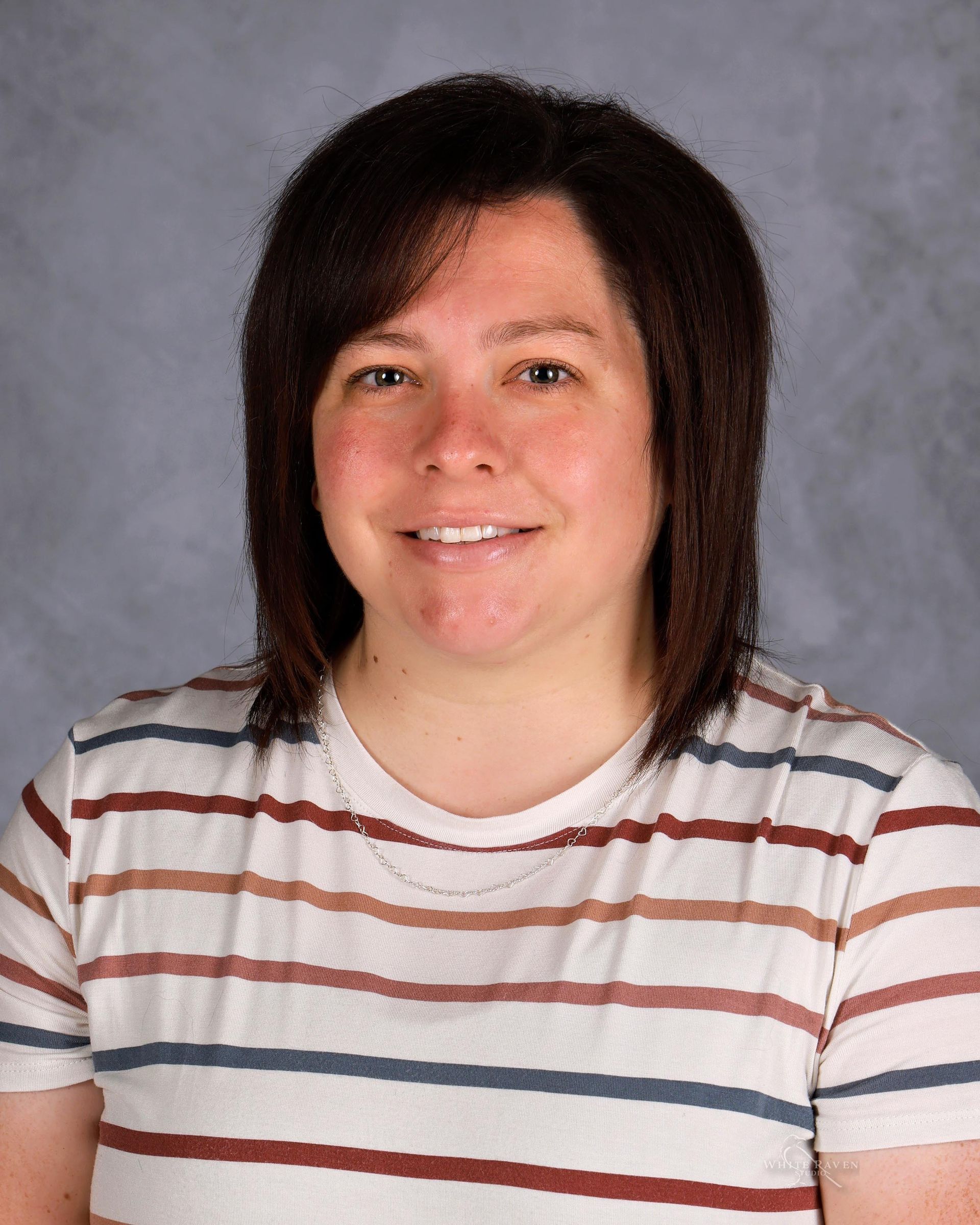 Woman smiling, wearing a striped shirt, brown hair with bangs. Background is a light blue gradient.