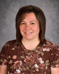 Studio portrait of a smiling person in a brown floral blouse against a gray backdrop