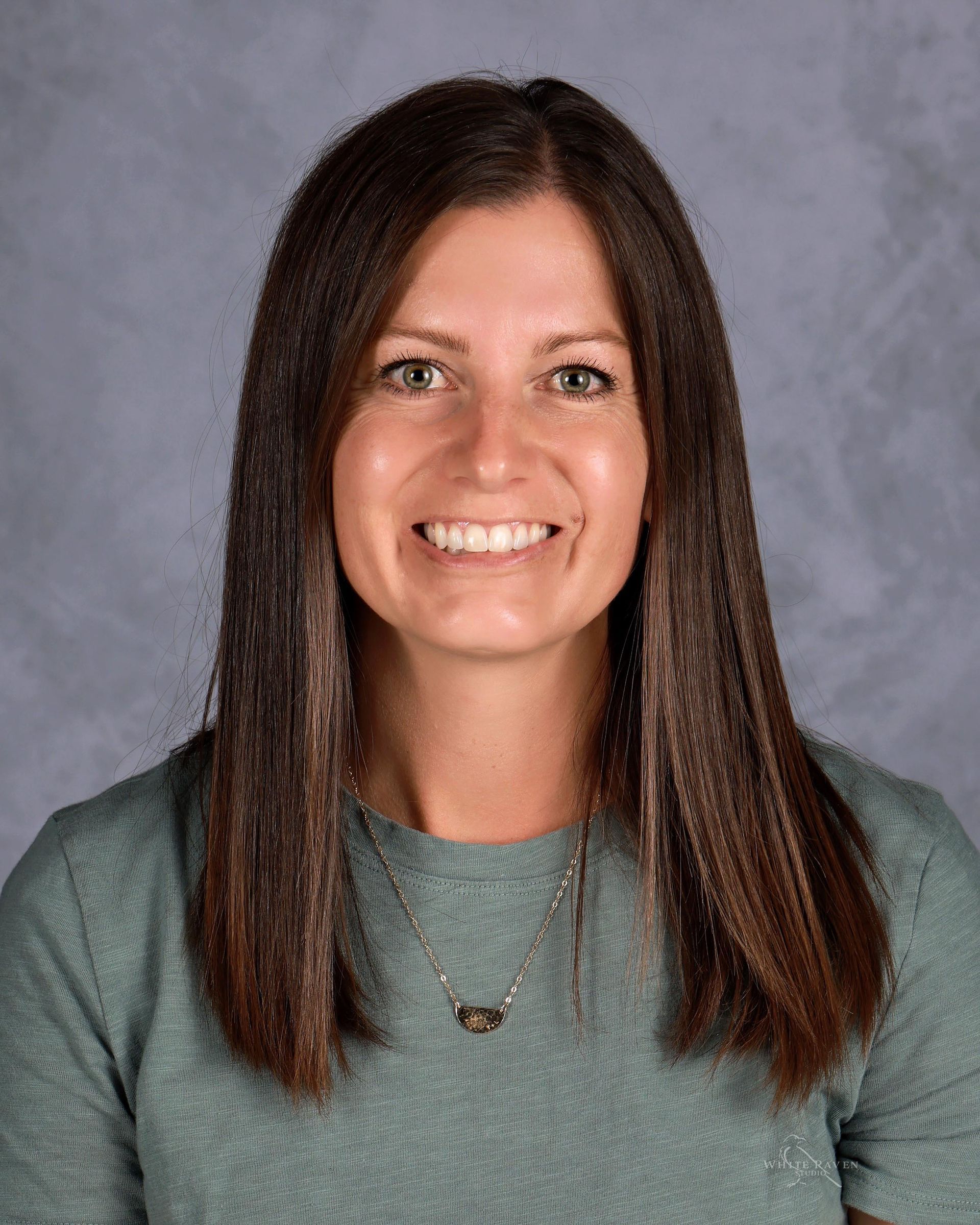 Woman with long brown hair smiling, wearing a teal sweater.