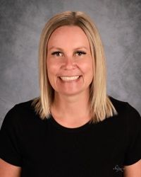 Smiling person with blonde hair in a black shirt against a gray studio backdrop