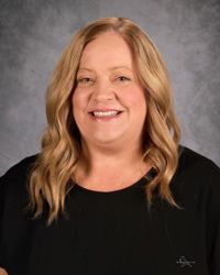 Smiling woman with wavy blonde hair wearing a black top against a gray studio backdrop