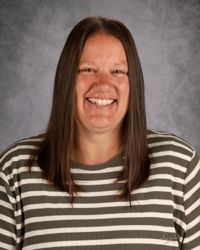 Smiling person with long brown hair wearing a black-and-white striped shirt against a gray backdrop