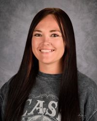 Smiling person with long dark hair in a gray shirt against a mottled gray background
