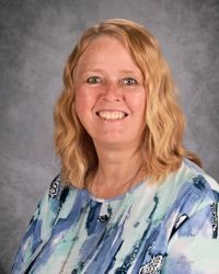 Smiling woman in a blue patterned blouse against a gray studio backdrop