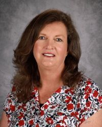 Smiling woman with brown hair in a red, white, and black floral blouse against a gray backdrop