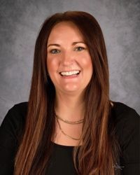 Portrait of a smiling woman with long brown hair against a gray studio backdrop