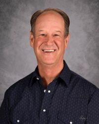 Smiling man in a dark blue button-up shirt against a gray studio backdrop