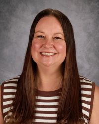 Smiling person with long brown hair wearing a striped shirt against a gray studio backdrop