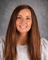 Smiling person with long brown hair against a gray studio backdrop