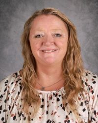 Portrait of a smiling woman with wavy blonde hair against a gray studio backdrop