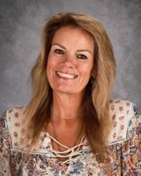 Smiling woman in a patterned blouse against a gray studio backdrop