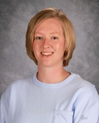 Smiling person in a light blue shirt against a gray studio backdrop