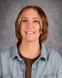 Portrait of a smiling person in a denim shirt against a gray studio background