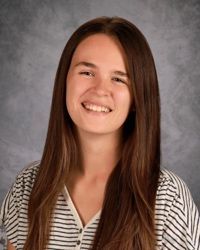 Smiling person with long brown hair in a striped top against a gray studio background