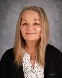Portrait of a smiling woman in a black cardigan over a white polka-dot blouse on a gray backdrop