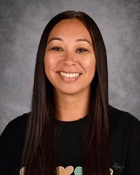 Smiling woman with long dark hair against a gray studio backdrop, wearing a black shirt.