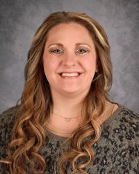 Portrait of a smiling woman with long wavy hair against a gray studio backdrop