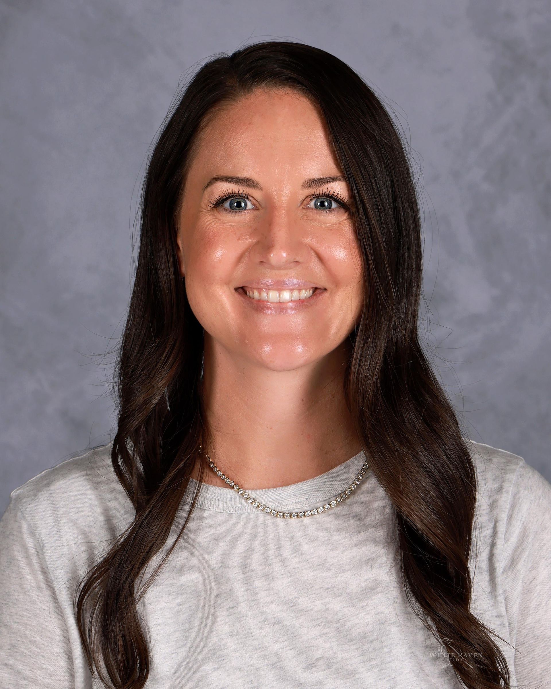 Woman with long, brown hair smiling, wearing a gray sweater.
