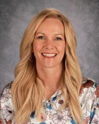 Smiling woman with long blonde hair in a floral blouse against a gray studio backdrop